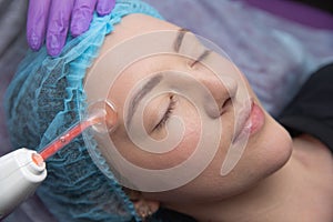 Receiving electric darsonval facial massage procedure at salon