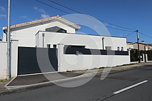 Recent white and gray house with a large protective wall and a dark gray automatic gate