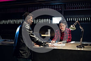 At the reception desk with a laptop, a young girl with tattoos helps a young black guy choose a tattoo sketch.