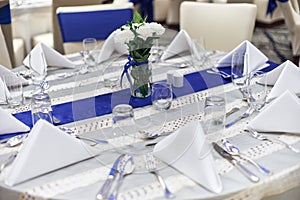 Reception dinner table setup with dinnerware, napkin, spoon, fork and glasses decoration with blue sash cloth stripe