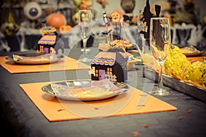 Reception table with a black tablecloth and decorations for halloween party, a small cardboard house, glasses and plates in carton