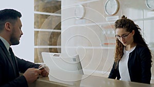 Receptionist girl at in hotel talking with arrived businessman about check-in and giving key card to man . Business