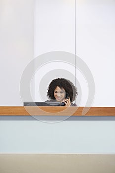 Receptionist Using Phone And Computer At Reception Desk