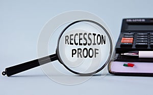 RECESSION PROOF - words on magnifying glass on a light background with calculator, notepad and pen
