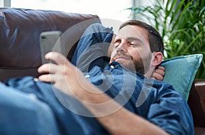 Recharge and bounce back better than ever. Shot of a young man using a smartphone while relaxing on a sofa.