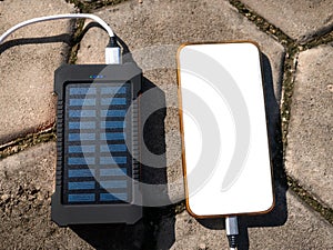 Rechargeable mobile power pack with solar panels, close-up. Connected to and charging a mobile, tablet or smart phone