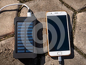 Rechargeable mobile power pack with solar panels, close-up. Connected to and charging a mobile, tablet or smart phone