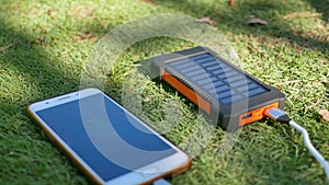 Rechargeable mobile power pack with solar panels on the lawn. Connected to and charging a mobile, tablet or smart phone. Solar pad