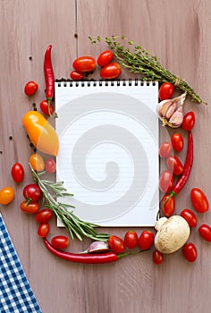 Recipe book with fresh vegetables and herbs on wooden.