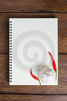 Recipe notebook, garlic, Red chilli on wooden background