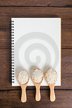 Recipe notebook, rice in wooden spoon on wooden background