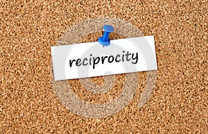 Reciprocity. Word written on a piece of paper, cork board background