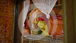 Reclining Buddha statue inside ornate temple with colorful murals. Sacred Buddhist imagery adorns walls. Tranquil