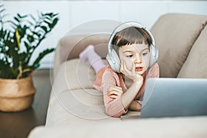 Reclining comfortably on a sofa, a cute 5-6-year-old girl watching a laptop screen, fully immersed in her digital world