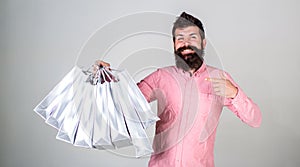 Recommendation concept. Hipster on smiling face recommends to buy. Guy shopping on sales season, pointing at bags. Man