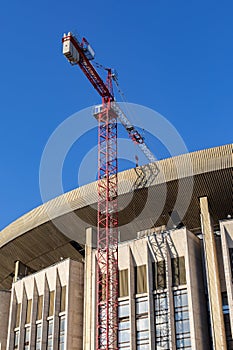 Reconstruction of a broken sports complex. The roof and facade of a large building, construction crane, vertical. Renovation