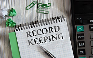 RECORD KEEPING - words on a white notepad on the background of a calculator, paper clips