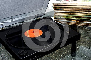 Record player with a vinyl record spinning with a stack of vinyls behind