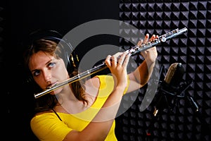 Record wind musical instruments with a professional microphone. Girl flute player in headphones plays in recording studio. Woman