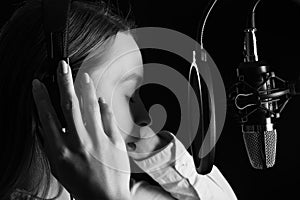 Recording female vocals. Young girl with a microphone and headphones in a recording studio. Vocal recording, blogger, reading text