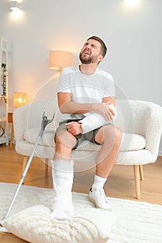 Recovery after physical injury in accident at home: Sad unlucky young man with broken leg, injured arm