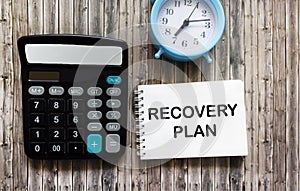 RECOVERY PLAN text in notepad on wooden table near calculator and clock, business concept