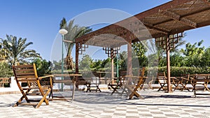 In the recreation area, under a lattice canopy, there are wooden chairs and tables