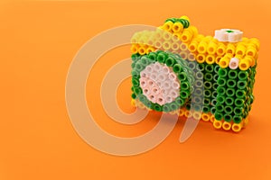 Recreation of a professional photo camera with an intense orange background made with green, white and yellow plastic rings