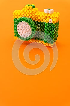 Recreation of a professional photo camera with an intense orange background made with green, white and yellow plastic rings