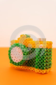 Recreation of a professional photo camera with an intense orange and pure white background made with green, white and yellow