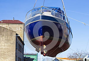 Recreational boat being lifted by heavy industrial crane machinery against blue sky background