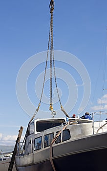 The boat being lifted by heavy industrial crane machinery against blue sky background