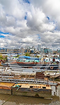 Recreational boats and some dilapidated ones moored on the bank of the River Thames at Butler\'s Wharf in London.