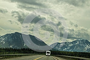 Recreational Vehicle driving on two lane blacktop highway toward mountains in Alaska range on rainy overcast misty day