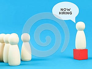 Recruitment new employees concept. Bubble speech now hiring with wooden dolls.