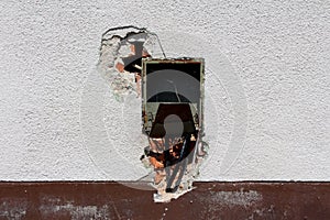 Rectangle empty plastic electrical outlet box with broken cover and cut wires mounted on cracked family house wall