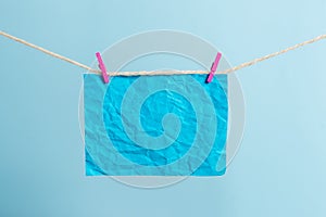 Rectangle shaped note colored paper clipped in a clothesline by clothespin in a white wooden background. Square empty