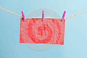 Rectangle shaped note colored paper clipped in a clothesline by clothespin in a white wooden background. Square empty