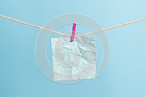 Rectangle shaped note colored paper clipped in a clothesline by clothespin in a white wooden background. Square empty