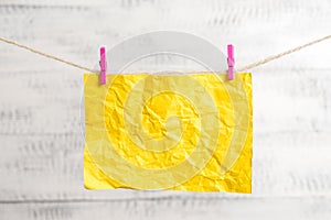 Rectangle shaped note colored paper clipped in a clothesline by clothespin in a white wooden background. Square empty