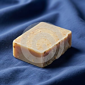 A rectangular bar of handmade soap rests on a crumpled blue fabric background