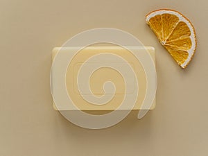 Rectangular bar of soap and slice of dried orange on beige background