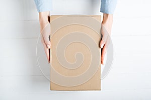 Rectangular cardboard box in female hands. Top view, white background