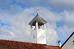 Rectangular catholic church bell tower with cross carved in white facade covered with dark metal roof and shiny new cross on top