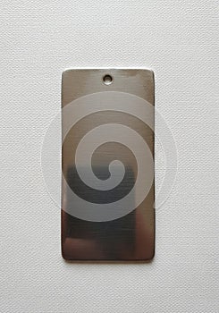Rectangular metallic tag with rounded corners, featuring a small circular hole near the