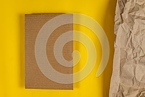 A rectangular piece of brown cardboard against a yellow background. Crumpled wrapping paper on the right side of the photo. Copy