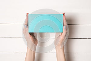 Rectangular turquoise box in female hands. Top view. White table on the background