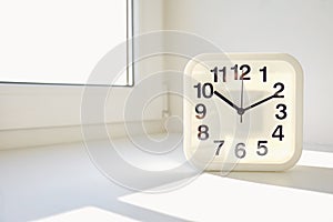 Rectangular white alarm clock on window background.