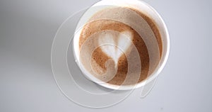 A recyclable eco cup in which hot cappuccino coffee with a heart pattern.