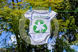 Recycle clothes icon on Babygro drying outside on washing line with 100% Recycled text photo